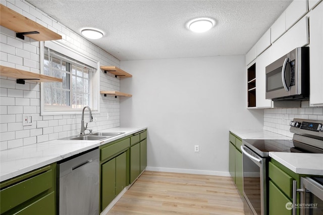 kitchen with green cabinets, appliances with stainless steel finishes, tasteful backsplash, light wood-type flooring, and sink