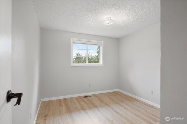 spare room with a textured ceiling and light hardwood / wood-style flooring