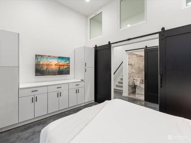 bedroom with a towering ceiling, ensuite bathroom, and a barn door