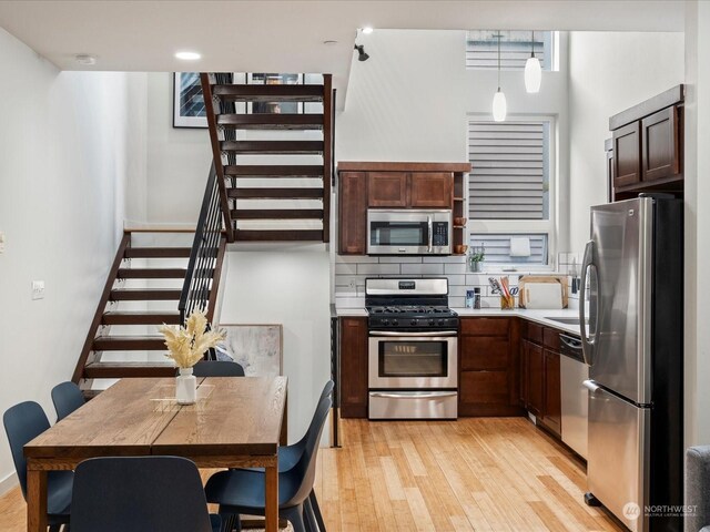 kitchen featuring light wood-type flooring, backsplash, dark brown cabinetry, pendant lighting, and appliances with stainless steel finishes