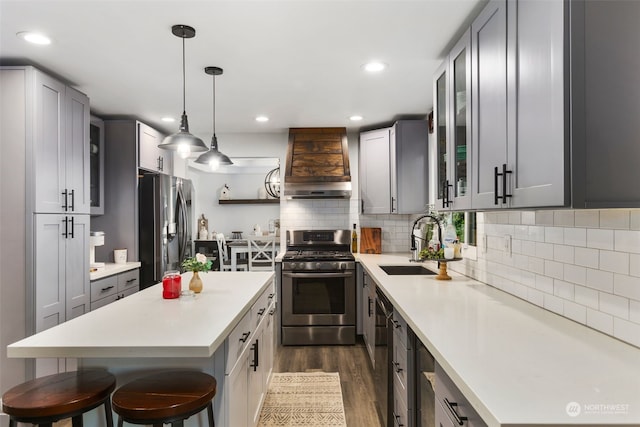 kitchen featuring appliances with stainless steel finishes, gray cabinets, custom range hood, and a kitchen bar