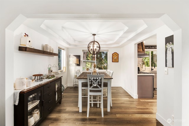 dining area featuring sink, an inviting chandelier, a tray ceiling, and dark wood-type flooring