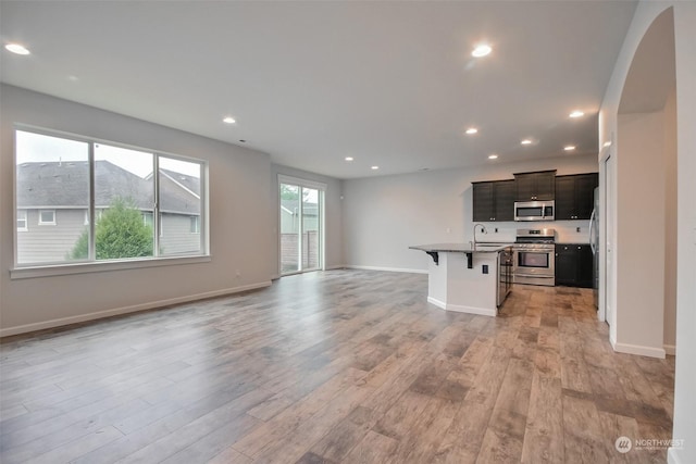 kitchen with light wood-style flooring, stainless steel appliances, a sink, a kitchen breakfast bar, and open floor plan