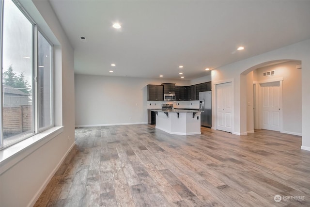 unfurnished living room featuring arched walkways, recessed lighting, visible vents, baseboards, and light wood-type flooring