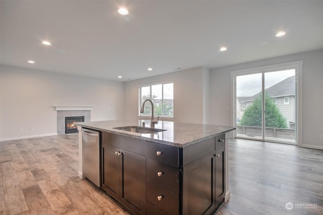 kitchen with dishwasher, light stone counters, light wood-type flooring, and a sink