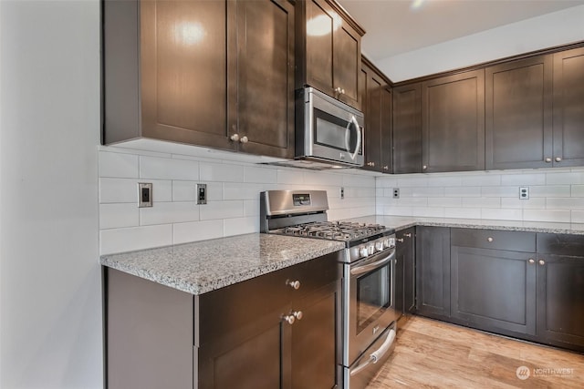 kitchen with light stone counters, backsplash, appliances with stainless steel finishes, dark brown cabinetry, and light wood-type flooring