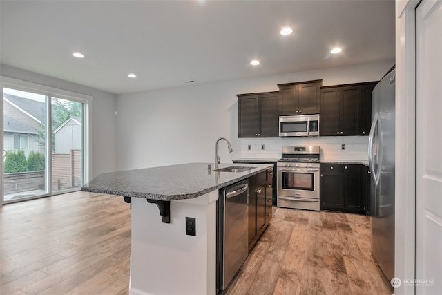 kitchen featuring light wood-type flooring, a center island with sink, stainless steel appliances, and decorative backsplash