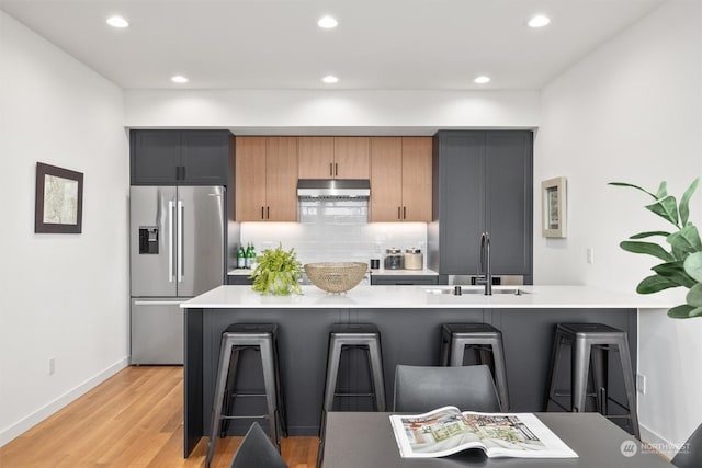 kitchen with backsplash, light wood-type flooring, stainless steel fridge with ice dispenser, and a breakfast bar area