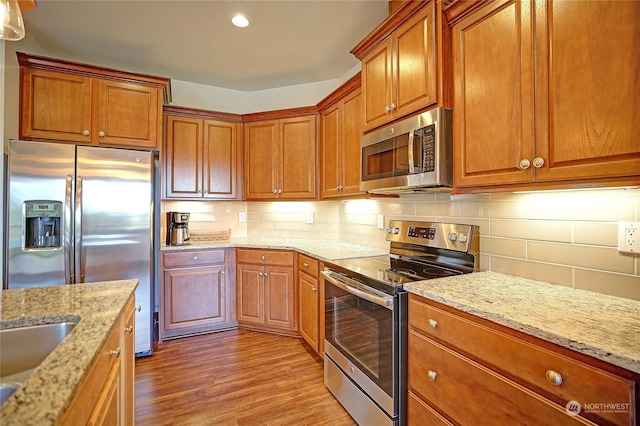 kitchen with sink, light stone counters, stainless steel appliances, light hardwood / wood-style floors, and decorative backsplash