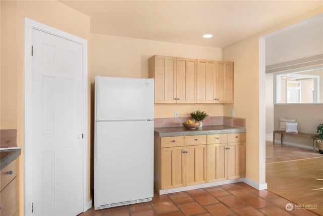 kitchen with dark tile patterned floors, light brown cabinetry, and white refrigerator