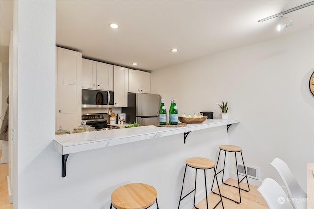 kitchen with kitchen peninsula, a kitchen bar, light wood-type flooring, white cabinets, and appliances with stainless steel finishes