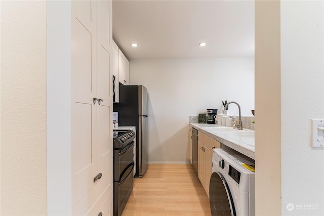 kitchen featuring washer / clothes dryer, white cabinets, light hardwood / wood-style floors, stainless steel appliances, and sink