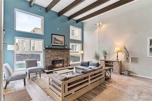 living room with wooden ceiling, beamed ceiling, a fireplace, a high ceiling, and light hardwood / wood-style flooring