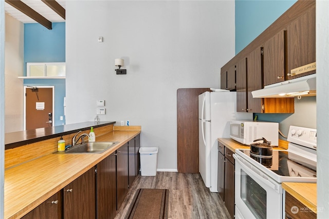 kitchen with white appliances, kitchen peninsula, beamed ceiling, dark wood-type flooring, and sink