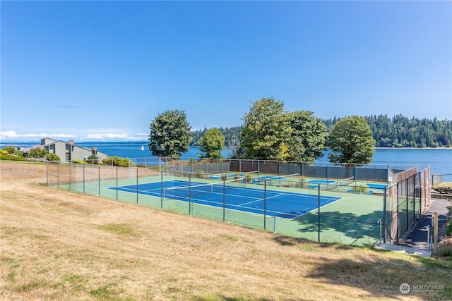 view of tennis court featuring a water view and a lawn