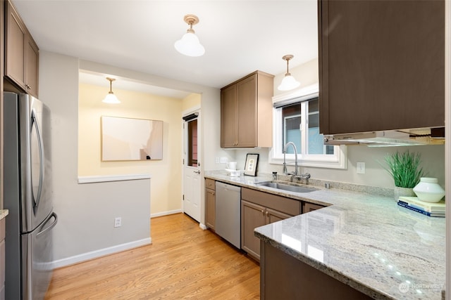 kitchen featuring light hardwood / wood-style floors, stainless steel appliances, hanging light fixtures, light stone counters, and sink