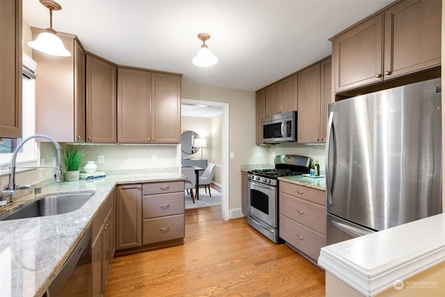 kitchen featuring appliances with stainless steel finishes, light wood-type flooring, pendant lighting, light stone counters, and sink