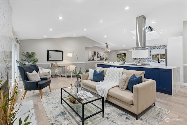 living room featuring sink, light wood-type flooring, and vaulted ceiling