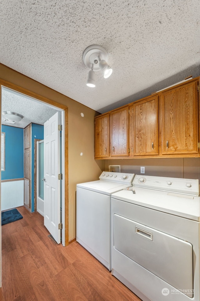 washroom with independent washer and dryer, cabinets, light hardwood / wood-style floors, and a textured ceiling