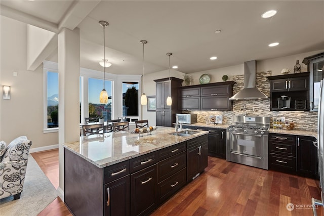 kitchen featuring high end range, backsplash, an island with sink, decorative light fixtures, and wall chimney exhaust hood