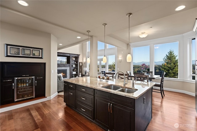 kitchen featuring sink, light stone counters, decorative light fixtures, a center island with sink, and hardwood / wood-style flooring