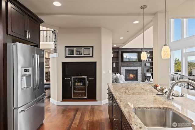 kitchen featuring stainless steel refrigerator with ice dispenser, wine cooler, dark brown cabinetry, sink, and light stone countertops