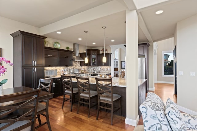 kitchen featuring pendant lighting, a breakfast bar area, backsplash, light wood-type flooring, and wall chimney exhaust hood