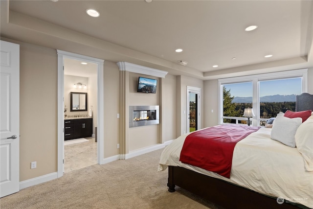 bedroom featuring connected bathroom, a tray ceiling, access to outside, and light colored carpet