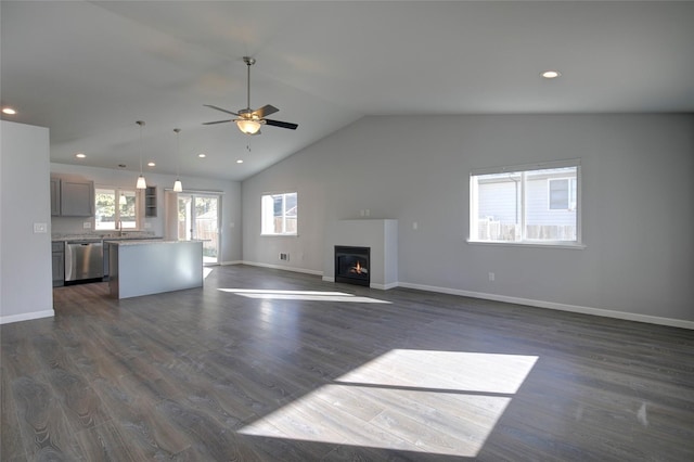 unfurnished living room featuring lofted ceiling, baseboards, dark wood finished floors, and a glass covered fireplace