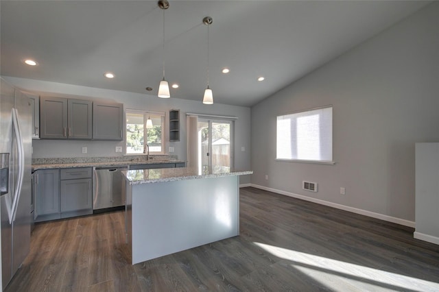 kitchen with light stone counters, stainless steel appliances, a sink, visible vents, and a center island