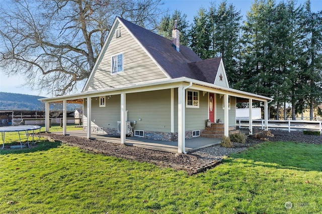 rear view of property with a trampoline and a yard