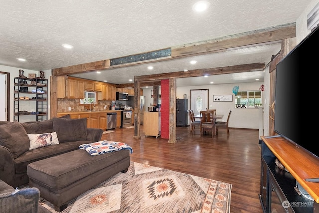 living room with a textured ceiling, dark wood-type flooring, beam ceiling, and a barn door