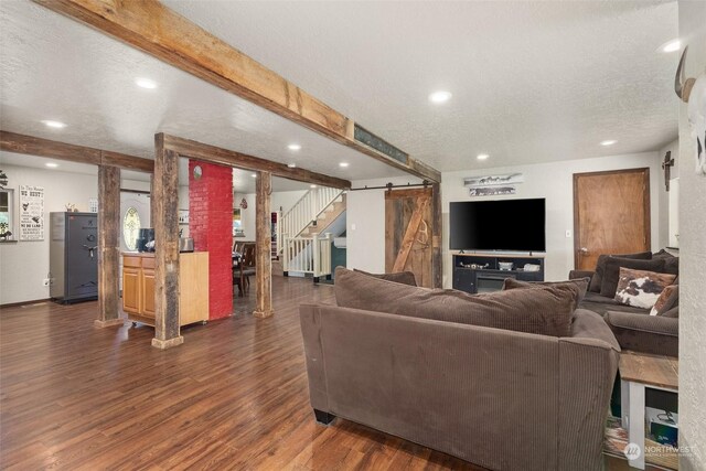 living room featuring dark wood-type flooring, a textured ceiling, beam ceiling, and a barn door