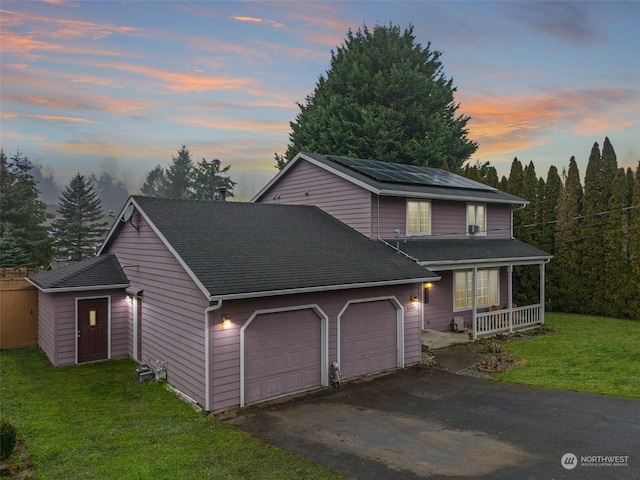 front of property with a porch, a garage, a yard, and solar panels