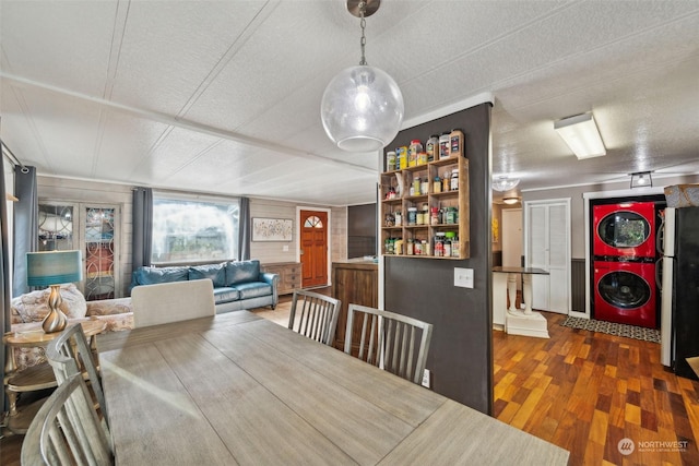 dining room featuring stacked washer and dryer, a textured ceiling, wooden walls, and dark hardwood / wood-style floors