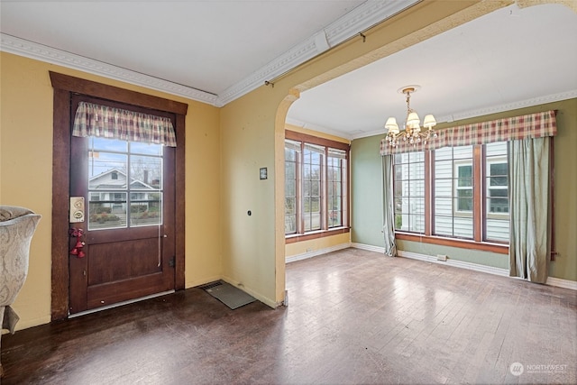 foyer with dark hardwood / wood-style flooring, an inviting chandelier, a wealth of natural light, and crown molding