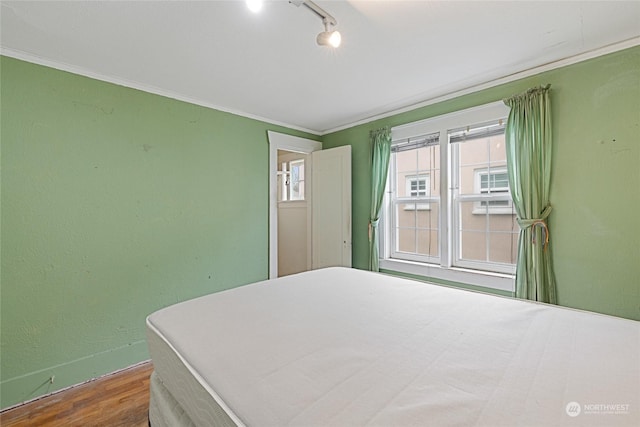 bedroom with rail lighting, hardwood / wood-style floors, and crown molding