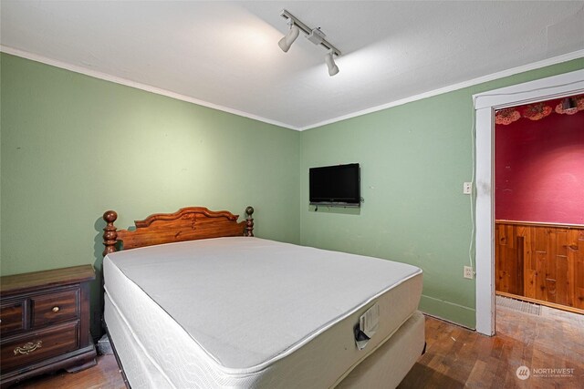 bedroom featuring dark wood-type flooring, track lighting, and crown molding