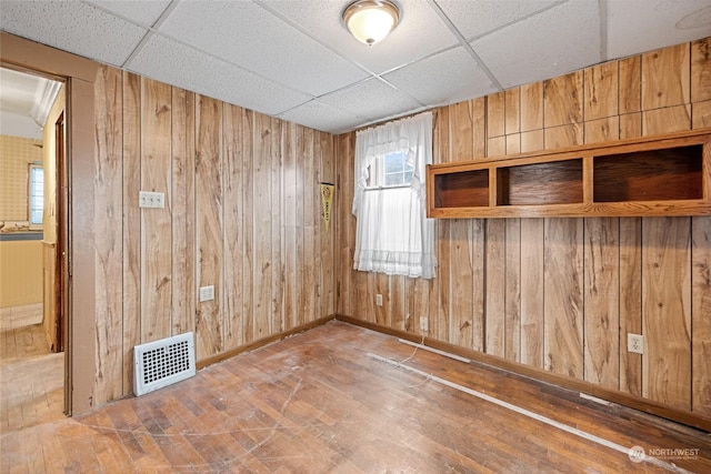 empty room featuring a paneled ceiling and wood walls