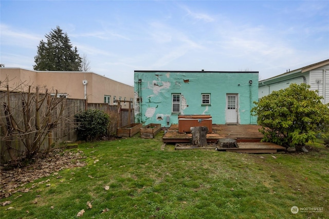 rear view of property with a deck, a lawn, and a hot tub