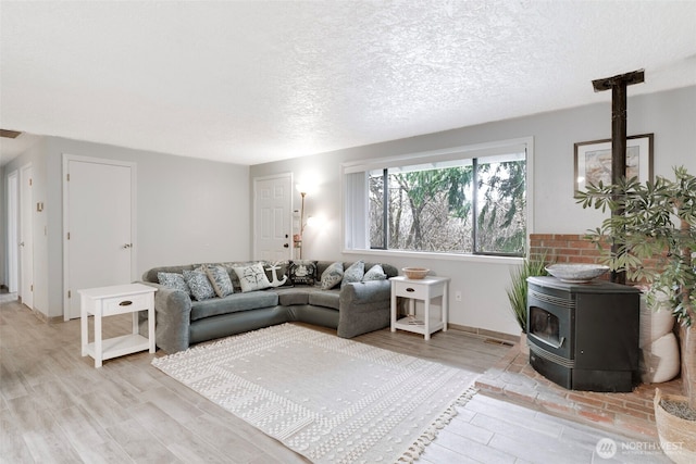 living room with a textured ceiling, visible vents, light wood-type flooring, and a wood stove