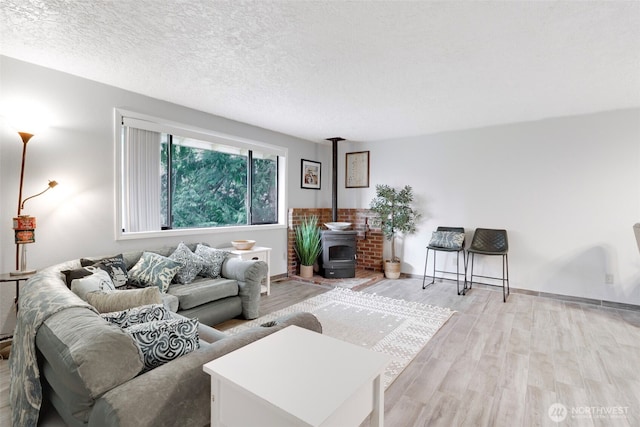 living area with a textured ceiling, light wood-type flooring, a wood stove, and baseboards