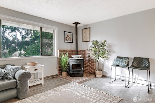 sitting room featuring a wood stove, a textured ceiling, baseboards, and wood finished floors