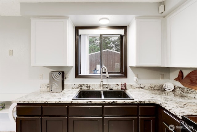 kitchen with black range with electric stovetop, white cabinetry, a sink, dark brown cabinetry, and light stone countertops