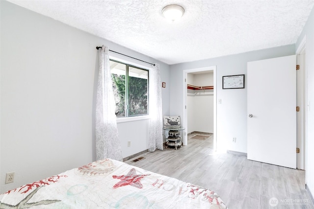 unfurnished bedroom featuring light wood finished floors, a closet, visible vents, a textured ceiling, and baseboards