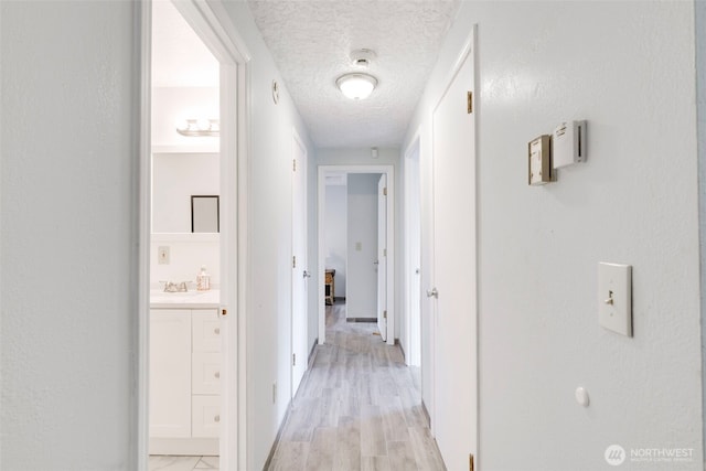 hall featuring a sink, light wood finished floors, and a textured ceiling