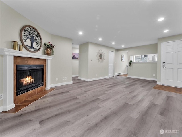 unfurnished living room featuring baseboard heating, light wood-type flooring, and a tiled fireplace