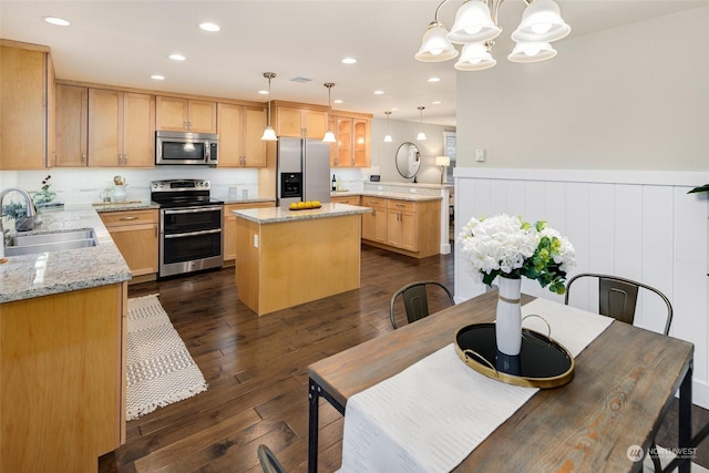 kitchen featuring decorative light fixtures, a kitchen island, sink, light stone countertops, and appliances with stainless steel finishes