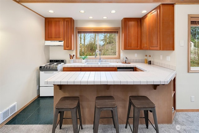 kitchen with electric stove, sink, kitchen peninsula, tile countertops, and a breakfast bar area