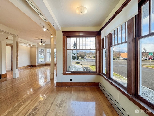 unfurnished room with a baseboard heating unit, decorative columns, and light hardwood / wood-style floors